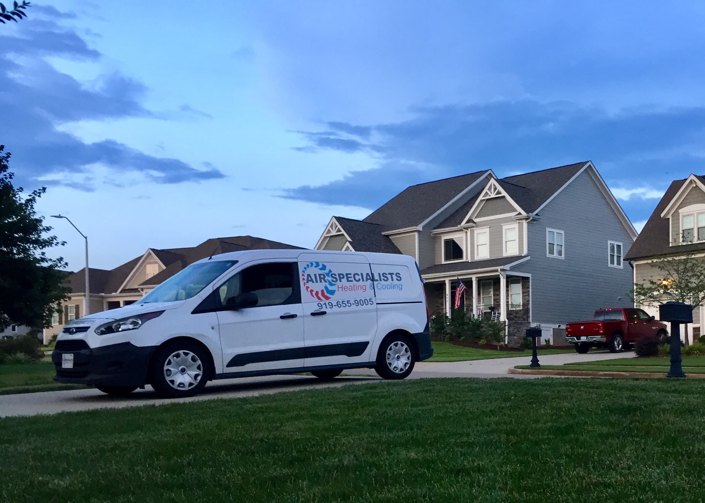 White Air Specialists Heating & Cooling van parked in a residential driveway at dusk.